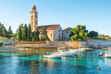 Turquoise water of Adriatic sea bay on Hvar island with franciscian monastery and boats in Dalmatia region, Croatia - obrazy, fototapety, plakaty