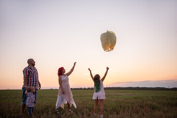 Concept of hope. Teamwork. Diversity family launch yellow sky lantern in field at sunset.