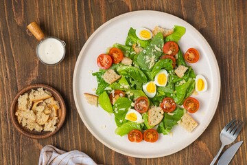 Caesar salad with romaine lettuce, cherry tomatoes, boiled quail eggs and croutons on a light ceramic plate on a wooden background. American cuisine