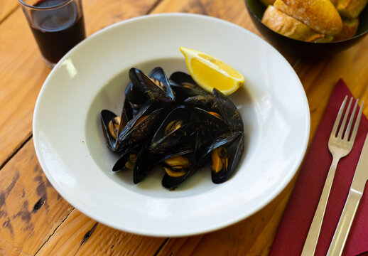 Portion of steamed mussels served on white plate with piece of lemon. Spanish dish mejillon al vapor
