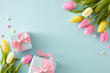 Mother's Day concept. Top view composition of gift boxes with bows colorful hearts and bouquets of flowers yellow pink tulips on pastel blue background with empty space in the middle