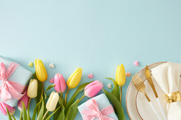 Happy Mother's Day concept. Top view photo of plate with cutlery and fabric napkin gift boxes colorful hearts and yellow pink tulips on isolated pastel blue background with empty space