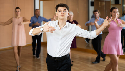 Interested young guy practicing movements of slow elegant wedding dance during group class in...