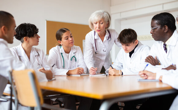 Elderly female doctor conducts training for interns of different ages at round table in auditorium of a medical university