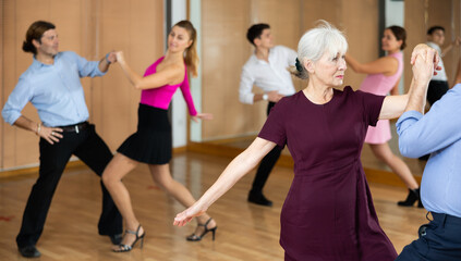 elderly couple in their free time is engaged in latin dance class and learns movements of cha-cha-cha dance