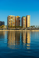 Buildings reflected in blue water in port in Malaga, Spain on January 14, 2023
