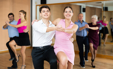 Fototapeta na wymiar Cheerful young guy and girl practicing ballroom dances in ballroom