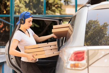 Woman delivering pizza to office by car side view, young fast food restaurant courier holding boxes...