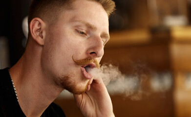 handsome young man with beard and mustache Vaping an Electronic Cigarette. hipster guy Exhaling Smoke Rings.