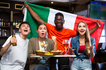 International sport fans waving Italian flag and supporting the national team while resting in the sport bar