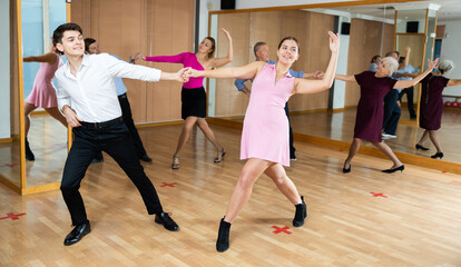 Cheerful young couple enjoying active dancing during group training in dance studio, practicing playful jitterbug movements