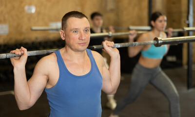 Fototapeta na wymiar Focused motivated sporty man performing set of exercises with barbell during intense group workout. Concept of weight training