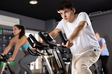 Motivated young guy leading healthy active lifestyle doing cardio workout on exercise bike in gym