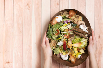Organic garbage for compost in female hands on a wooden background. Composting concept flat lay,...