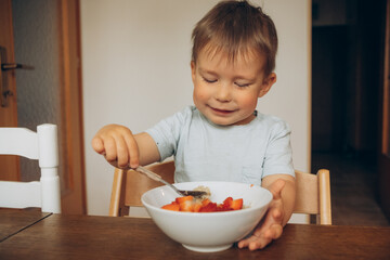 child eating oatmeal with strawberries at the table at home