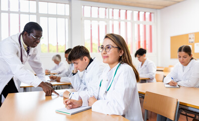 Young latin woman medical student in white coat attedning classes in university, sitting at desk and listening to lecture.