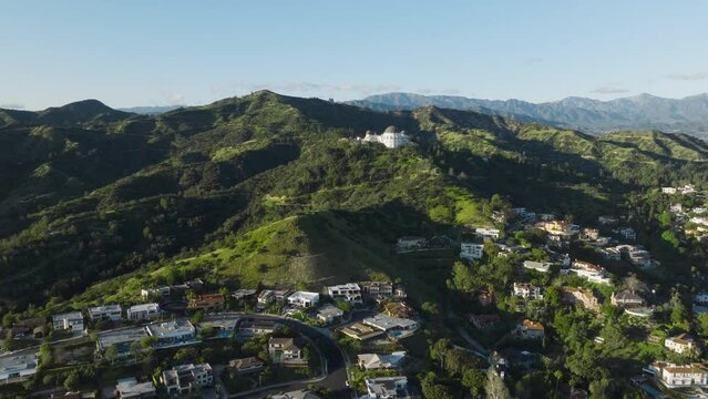 Large luxury villas and houses in Hollywood Hills in Los Angeles. Aerial of Los Feliz neighborhood area on sunny spring day with Griffith park and Observatory seen in distance on green hills 4K