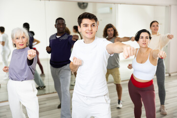 Fototapeta premium Smiling young guy standing in attacking stance, practicing movements of close combat punches in training room during self-defence workout