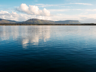 Benbulben mountain and blue water surface of Atlantic ocean with reflection of blue cloudy sky. Irish nature. County Sligo, Ireland. Popular tourist attraction. Stunning scenery.