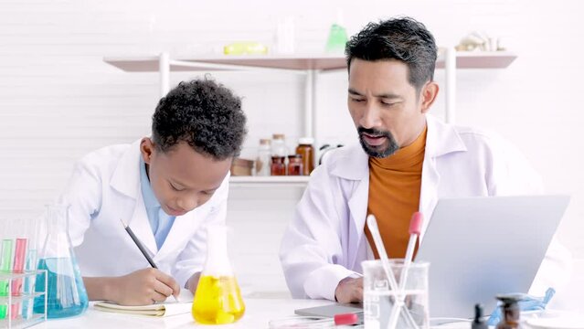 Teacher in white gown and student scientists making experiment in lab, teaching and guiding in his elementary school in science class. Happy african boy learning in chemistry class with professional