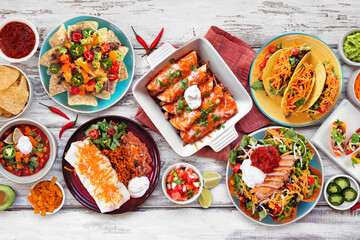 Mexican food table scene. Top view on a white wood background. Tacos, burrito plate, nachos,...