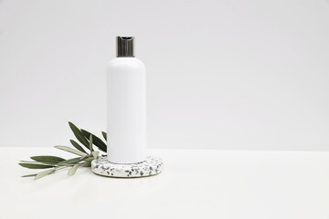 Cosmetic product mockup on white background. Plastic pump bottle for shampoo, lotion template. Stone terrazzo podium.Green olive tree branch. Healthy cosmetology, spa treatment concept. Copyspace