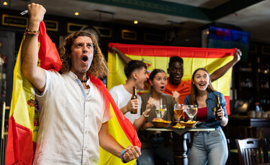 Naklejka premium Happy international sport supporters holding up the flag of Spain and drinking beer in the pub