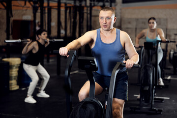 Portrait of concentrated adult man doing cardio training, cycling on stationary bike in gym. Sport and fitness concept..