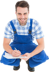 Happy repairman crouching while writing on clipboard