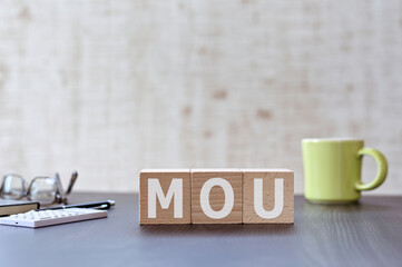 There is wood cube with the word MOU. It is an acronym for Memorandum of Understanding an eye-catching image.