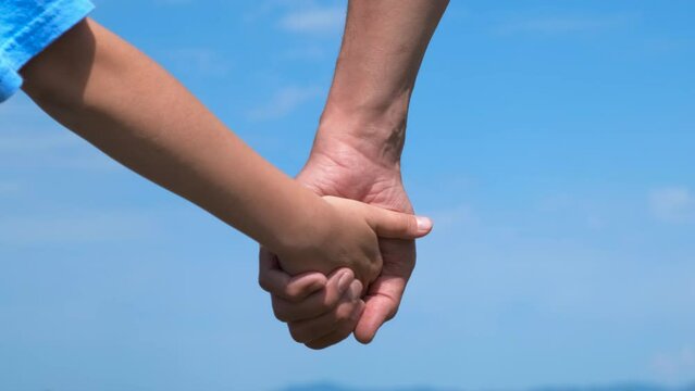 Friendly mum and child hand by sky. A child hol her mother's hand against blue sky. A concept of friendly family emotions outdoor.
