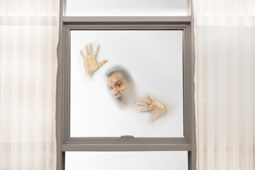 Screaming male face with hands pressed against window from a foggy background