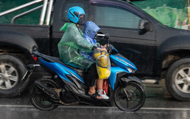  A woman with kid rides a motorcycle on the street in heavy rain