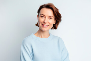 Smiling happy woman in her 40s wearing sky blue sweater with short brown hair on white background.