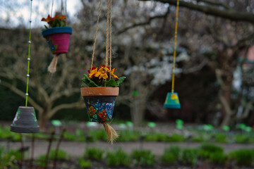 colorful ceramic pots painted in spring patterns hanging on a tree on strings in the garden