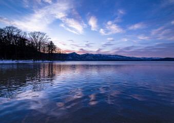 湖畔の森の木々と山と空を水面に反射する夜明けの湖。日本の北海道の屈斜路湖。