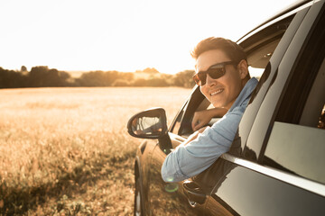Handsome young man sitting in car smiling looking out window 