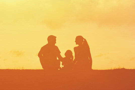 silhouette of happy family sitting together at sunset