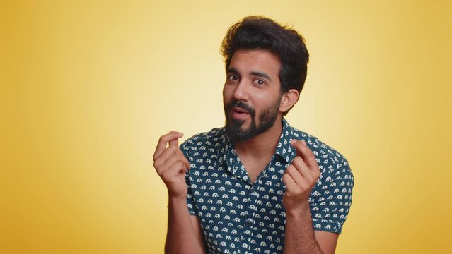 Young indian man showing wasting, throwing money around, more tips, big profit, winning lottery jackpot, successful shopping payment purchase, cashback. Hindu guy isolated on studio yellow background
