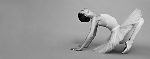 Young ballerina practicing dance moves on light grey background. Black and white effect. Banner...