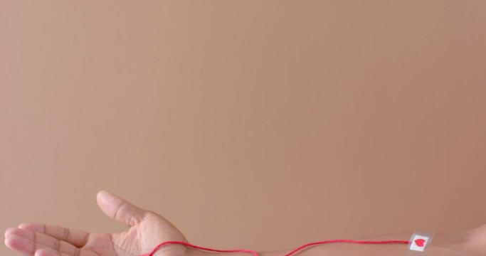 Hand of biracial man with blood drop, red string and heart sticking plaster on beige, slow motion
