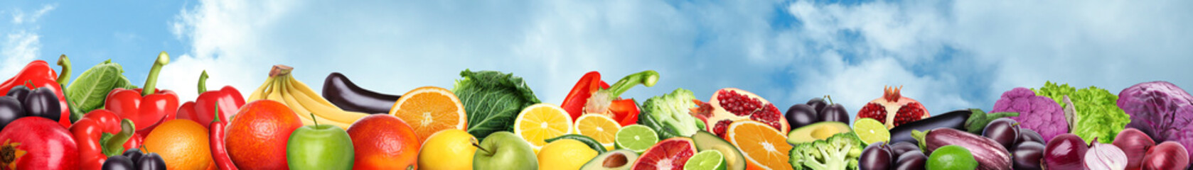 Many different fresh fruits and vegetables against blue sky with clouds. Banner design
