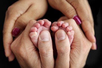 Feet of a newborn baby in the hands of parents. Happy Family concept. Mum and Dad hug their baby's legs. Studio photography on black background of a child's toes, heels and feet. 