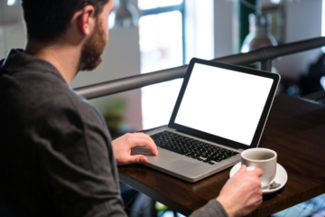 Man holding coffee cup and using laptop