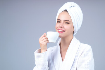 Morning coffee. Portrait of smiling woman with cup of drink coffee. Smiling girl drinking coffee isolated on gray studio background. Pretty woman in bathrobe and towel with cup of hot coffee.