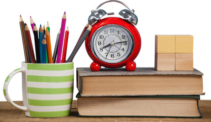 Alarm clock and books by colored pencils in mug on table