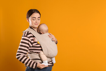 Mother holding her child in sling (baby carrier) on orange background. Space for text