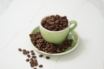 Medium sized green coffee cup filled with whole roasted coffee beans