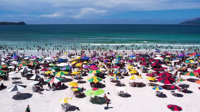 Vista do drone sobre a praia com dunas cheia de turistas e guarda-sol, mar limpo e areia branca na ver&atilde;o na cidade de Cabo Frio, Rio de Janeiro, Brasil