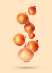 Many onion bulbs falling on beige background